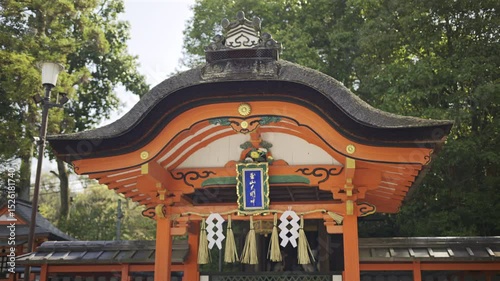 Red buildings of a historic shrine. The site features vibrant colors and intricate designs representing Japanese culture. Text translation: ''Okami Shrine