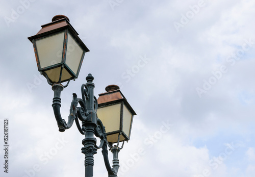 Elegant street lamps adorn a city street under a cloudy sky in the late afternoon