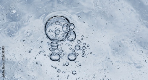 A close-up of a single, transparent, spherical object floating in a liquid, surrounded by smaller bubbles. 
