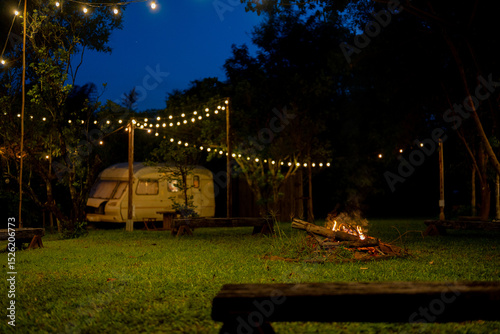 Cozy Night Campfire by Vintage Trailer with String Lights in Garden