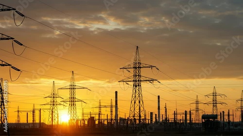 Silhouetted power lines and industrial structures at sunset.