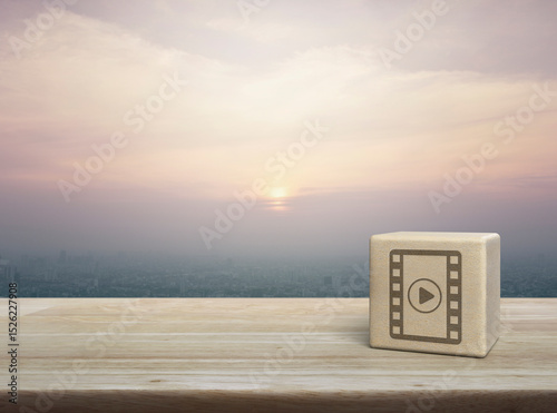 Play button with movie icon on wood block cube on wooden table over city tower and skyscraper at sunset, vintage style, Business cinema online concept