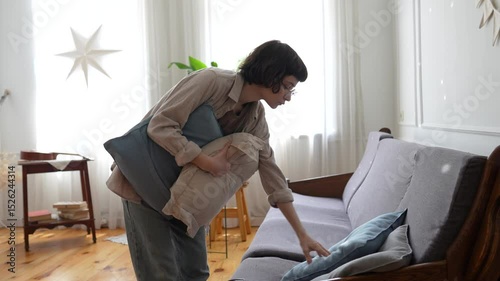 Focused housewife adjusting textile elements for balanced living space appearance. Interior refreshment with cushions, decorative alignment, household care, visual harmony, residential comfort
