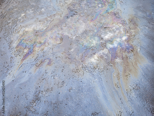 A multi-colored gasoline stain on the road on the melted snow.