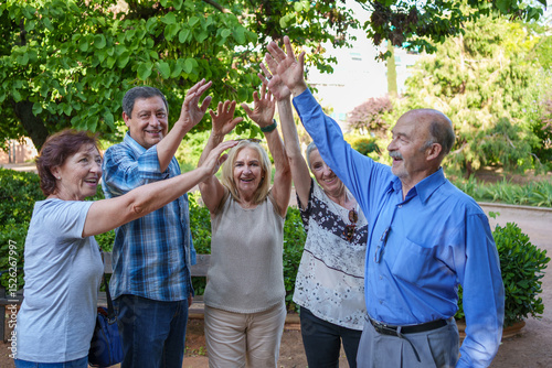 Group of senior friends joining hands in a park celebrating friendship and success