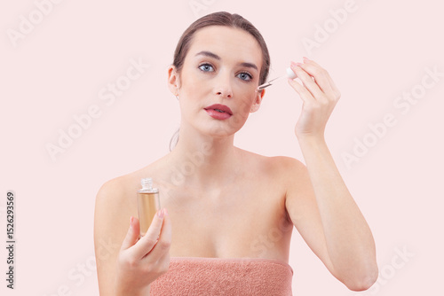 Woman applies serum to her face using a dropper. Radiating a sense of relaxation and self care. Isolated pink Background emphasizes the clean and fresh feeling associated with skincare routines