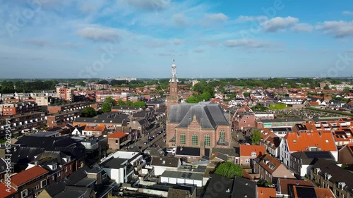 Aerial view of a Dutch town with a prominent church in the center, surrounded by residential homes, green trees, and a clear blue sky on a bright spring day. Peaceful and charming atmosphere.