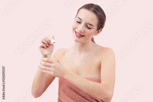 Smiling woman applies serum to her face using a dropper. Radiating sense of relaxation and self care. Isolated pink Background emphasizes the clean and fresh feeling associated with skincare routines
