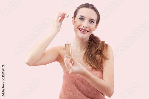 Smiling woman applies serum to her face using a dropper. Radiating sense of relaxation and self care. Isolated pink Background emphasizes the clean and fresh feeling associated with skincare routines