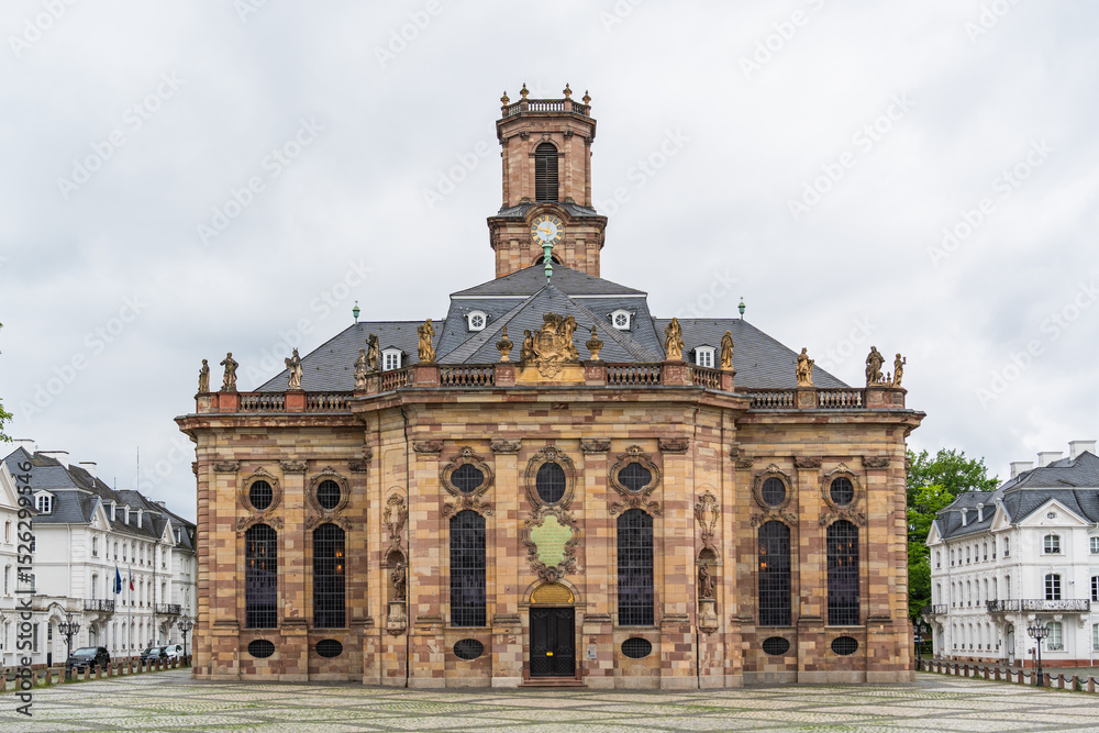 Obraz premium A large building Baroque church in the city of Saarbrucken in Germany with a clock tower and a small courtyard in front of it