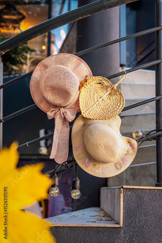 Straw hats hanging on railing. Three straw hats in different styles hang on metal railing outside near entrance, warm sunlight. Concept of summer end, change of seasons, arrival of autumn, nostalgia