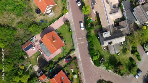 A stunning aerial view of a quaint European town, showcasing narrow streets, red-tiled rooftops, parked cars, and festive decorations stretching between charming houses.