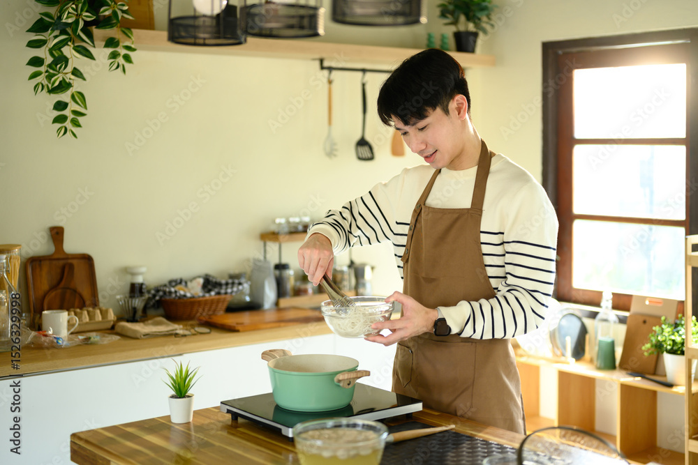 Fototapeta premium Young man in an apron preparing food on a stovetop, enjoying his time in the kitchen