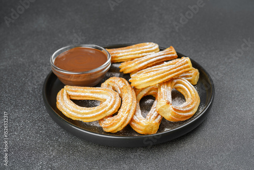 Traditional spanish dessert churros, fried dough pastry dusted with powdered sugar and chocolate sause on black background. Street food, sweet snack, homemade dessert.
