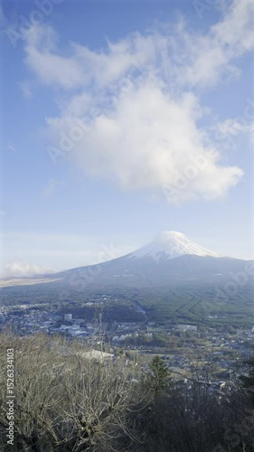 Snow-covered Fuji mountain rising above a peaceful town, illuminated by the soft glow of early morning sunlight against a clear blue sky. Vertical video