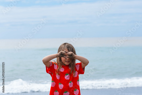 Beautiful little girl in red t-shirt looking at camera through binoculars in her hands