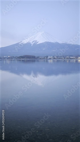 Snow-capped Fuji mountain over a tranquil lake, creating a stunning reflection in the still water. The scene captures the beauty of nature during twilight hours. Vertical video