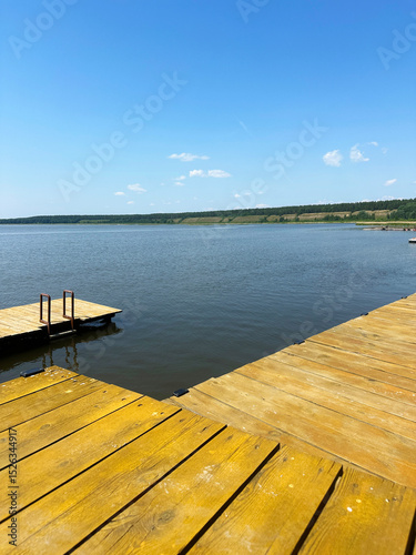 Wooden dock extending over tranquil summer lake under clear blue sky