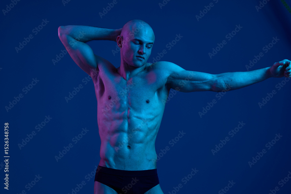 Obraz premium Athletic man posing in vibrant lighting, showcasing strong physique and confident expression. The image captures a playful and dynamic moment in a visually striking setting.