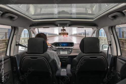 Car interior with panoramic roof. Driver in rain. Rear view.