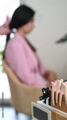 Vertical video of a hairdresser using a massage comb to gently brush a client’s hair in a salon