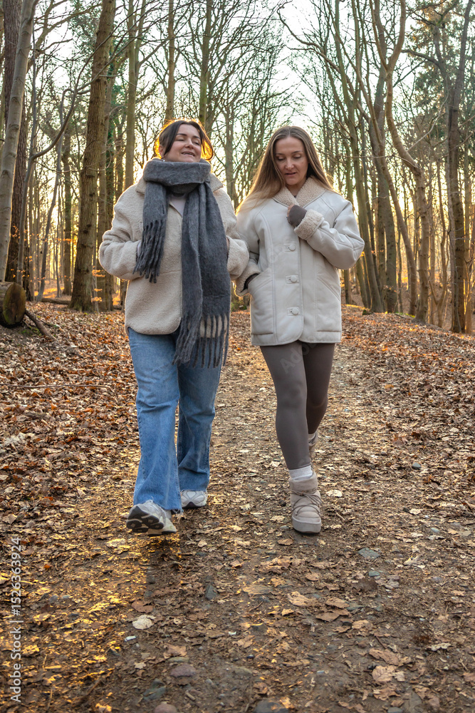 Fototapeta premium Two female friends on a walk in the forest. Friends walking through the forest. People in nature.