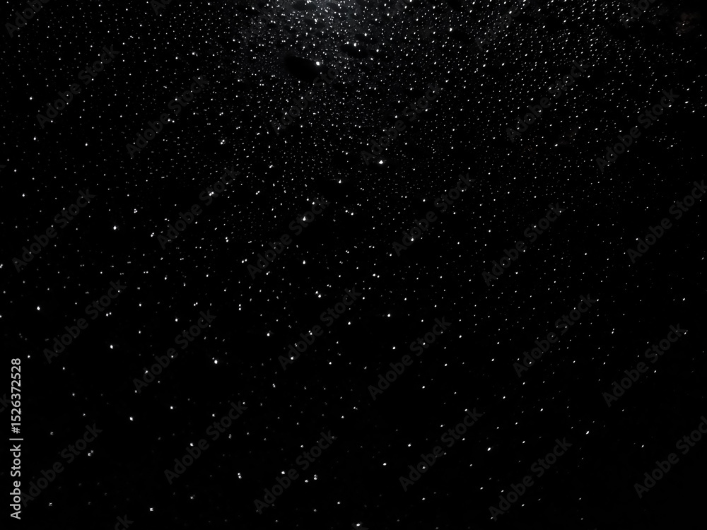 Fototapeta premium Raindrops on a dark car hood reflecting city lights. Abstract night shot resembling a starry sky with moisture and sparkle.