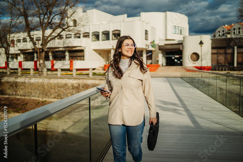 Young caucasian woman walk home from work drink coffee and use smartphone
