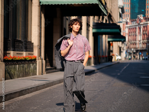 Portrait of handsome Chinese young man wearing gray suit walking in the street, young guy with black curly hair with urban background. Male fashion, cool Asian young man lifestyle.