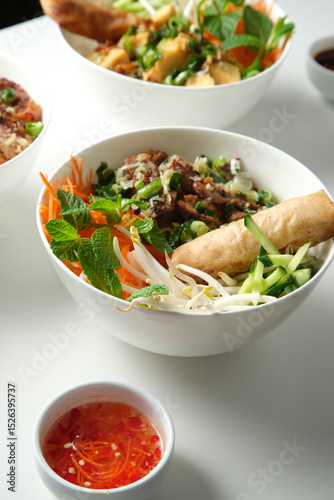 Bun Cha Gio bowls on a white countertop with a small dish of chili sauce on the side.