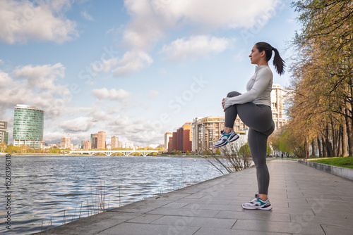 Sporty Woman Stretching Outdoors by the City Waterfront at Sunrise