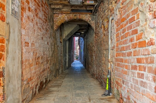 Venice, Italy - Narrow passage with brick walls leading to an arch in Venice