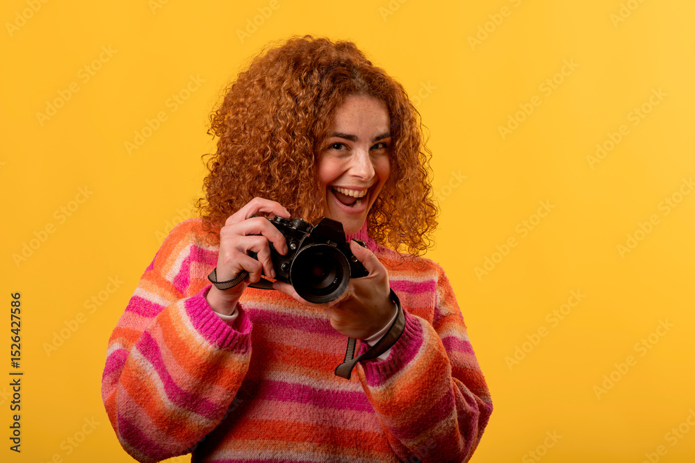 Obraz premium Enthusiastic photographer smiling and holding a camera in studio with yellow background