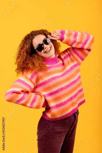 Redhead girl with sunglasses and striped sweater smiling on yellow background