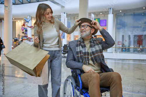Mature man in a wheelchair is assisted by a woman in a shopping mall