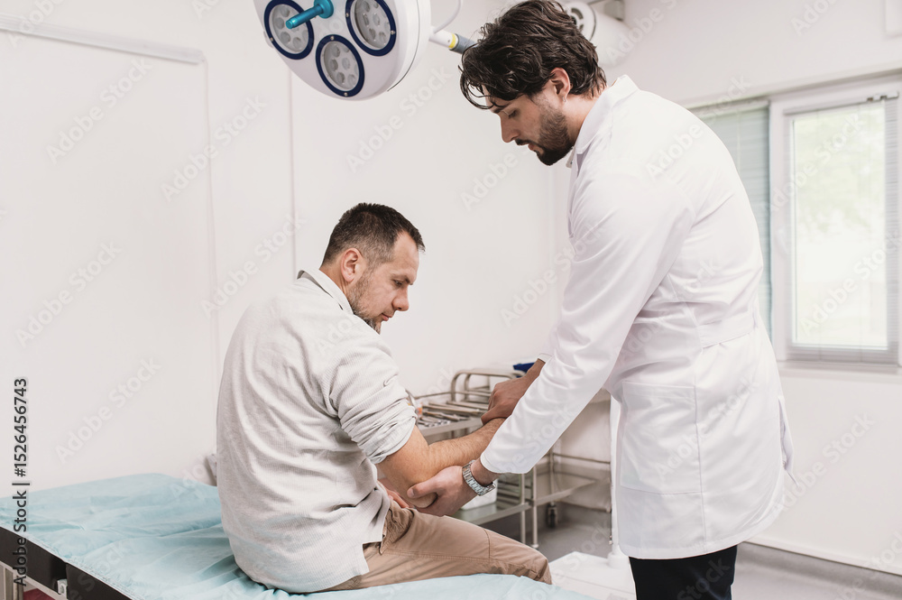 Obraz premium traumatologist examines male patient's elbow in hospital on couch in emergency room. range of motion test, pain, arm injury. Arthritis and joint problems, arthrosis, bruise, broken arm vertical