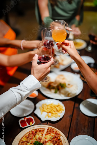 Close-up of friends sharing a delicious meal and drinks at a lively dinner party, featuring seafood, fries, and wine on a wooden table