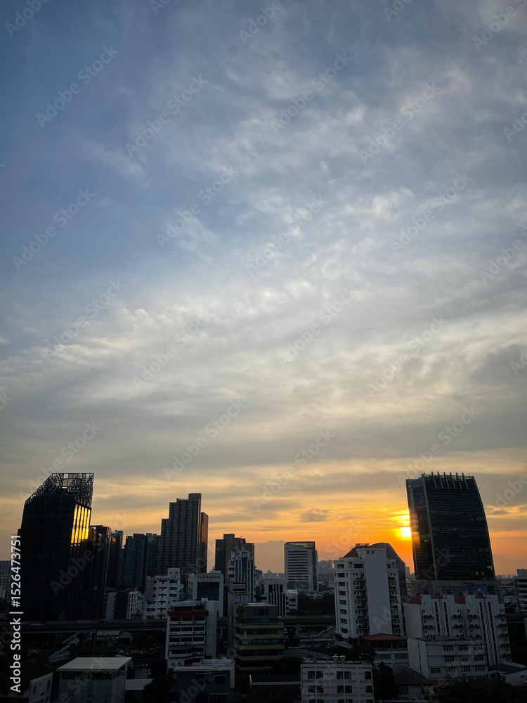 Obraz premium A city skyline at sunset with tall buildings silhouetted against a colorful sky filled with scattered clouds.