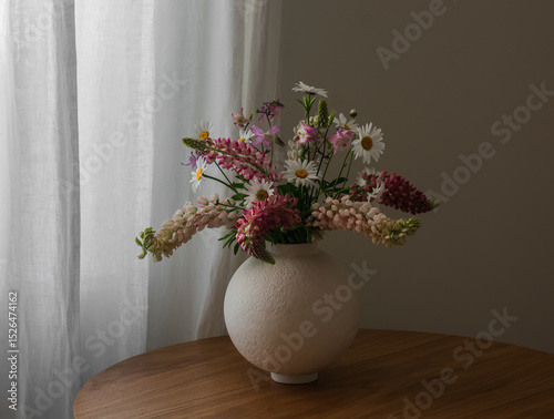 Summer bouquet of garden wildflowers, daisies, lupines in a ceramic vase on a wooden table