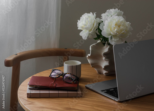 Home office - laptop, notebooks, a glass of coffee, a vase with peonies on a wooden table in the living room