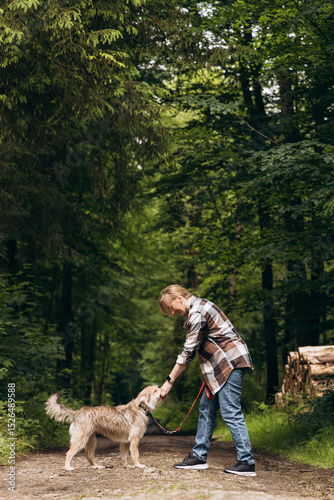 Person walking with a dog on a forest path, surrounded by lush greenery and tall trees, enjoying a peaceful outdoor moment together