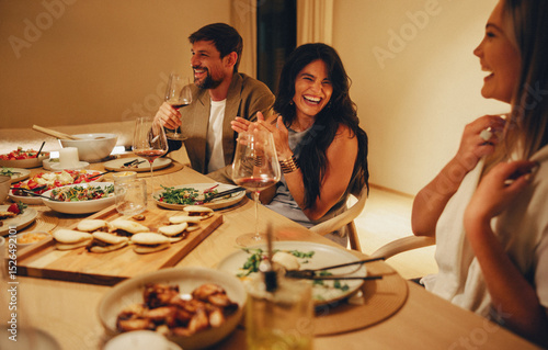 Friends laughing and enjoying dinner with wine and shared plates at home photo