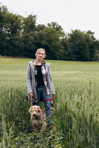Woman walking with a small dog through a lush green field, enjoying nature and companionship in a serene outdoor environment