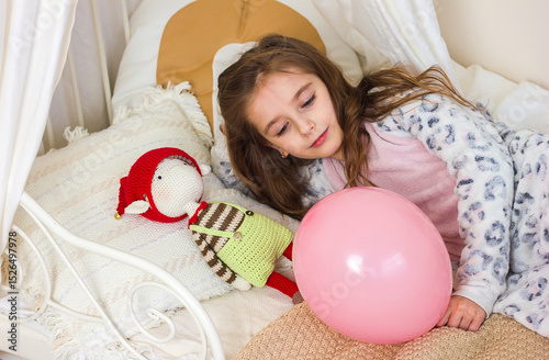 Beautiful little girl in kigurumi pajamas on the bed with her favorite knitted toy