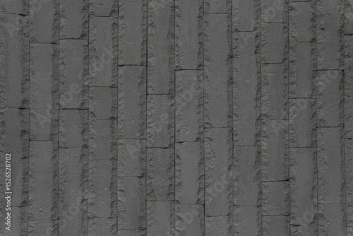 Vertical black bricks with broken edges form a vertical impregnable wall. Abstract architectural background.