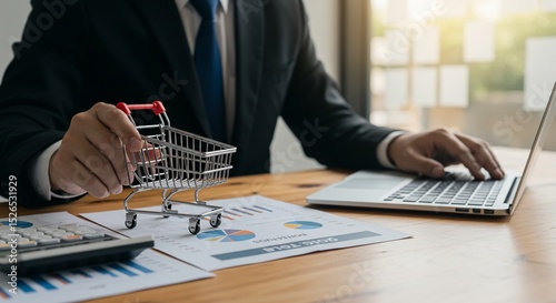 Online Shopping Analysis: Businessman with Miniature Cart and Laptop on Wooden Desk