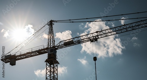 Tower crane silhouette against a bright sky with scattered clouds and sun flare