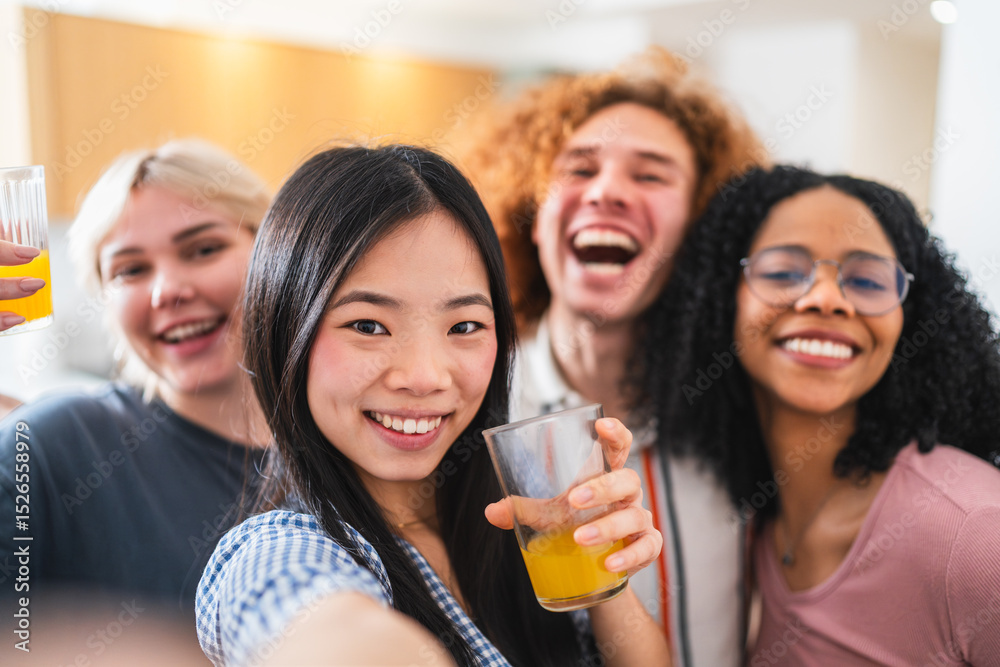 Obraz premium Group of cheerful young multiethnic friends enjoying a lively moment while taking a selfie and sipping refreshing juice in a cozy kitchen