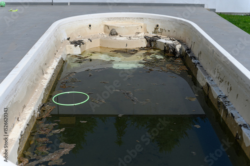 Dirty abandoned swimming pool with stagnant water and debris.