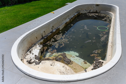 Dirty abandoned swimming pool with stagnant water and debris.